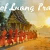 朝の光の中、ルアンパバーンの寺院の前を歩く僧侶たちの托鉢の様子。「Soul of Luang Prabang」の文字入り。この神聖な儀式は街の魂を象徴する観光の目玉であり、見学にはルールと敬意が求められます。