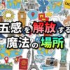 モロッコの古都マラケシュ、ジャマ・エル・フナ広場をイメージしたカラフルなイラスト。世界各地のランドマーク、地図、航空機、パスポート、カメラ、スーツケースなどが散りばめられ、「五感を解放する魔法の場所」という日本語のタイトルが中央に大きく配置されています。